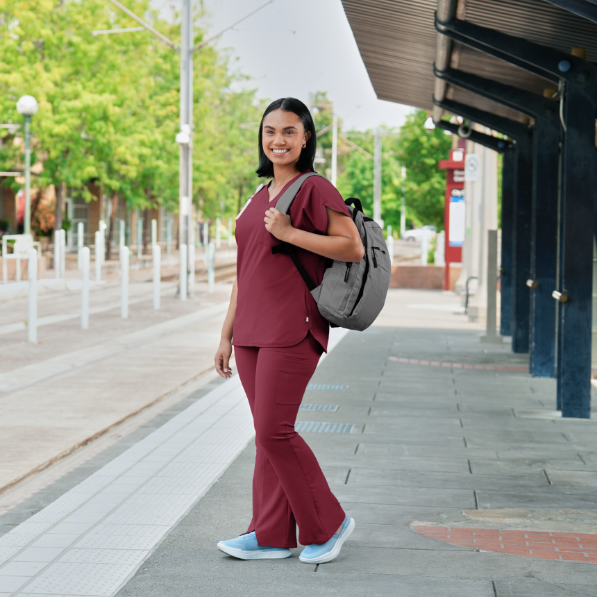 Woman in wine scrubs with a backpack standing on a sidewalk