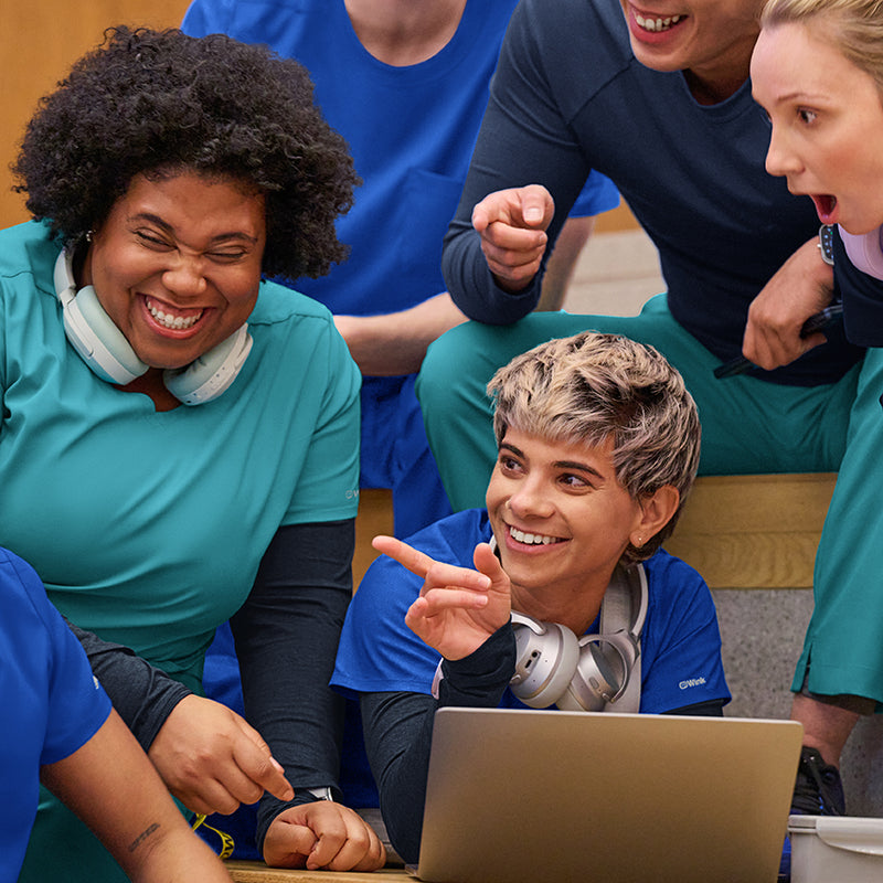 Group of nursing students gathered around a laptop, smiling and engaged in a shared activity.