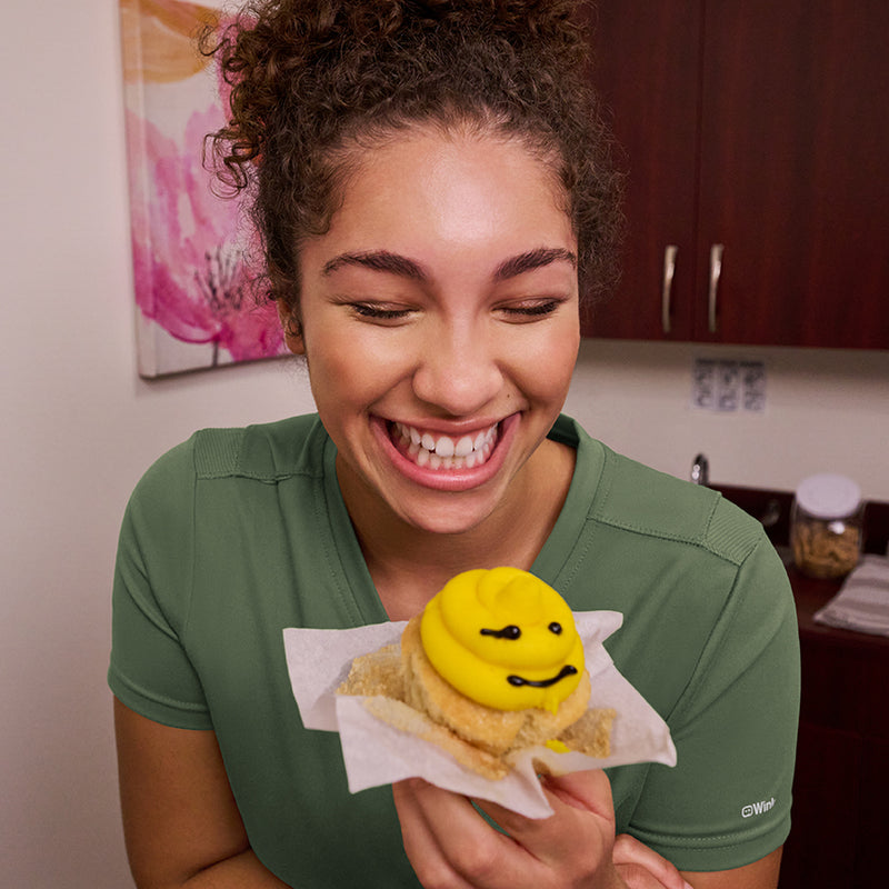 woman in green scrubs eating a cupcake