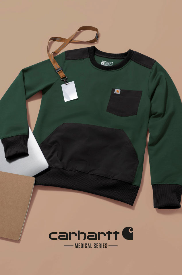 A Carhartt Medical Series sweatshirt in forest green and black, styled flat-lay with a brown leather lanyard, a white tag, a white laptop, and a brown folder on a beige background. The Carhartt brand logo is visible at the bottom of the image.