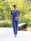 Person in galaxy blue scrubs walking outdoors with a coffee cup.