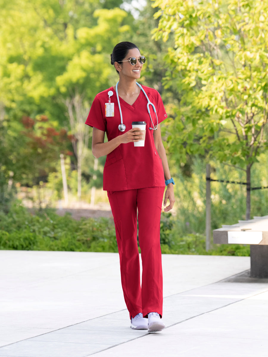 Nurse in red scrubs walking outdoors holding a coffee cup