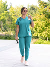 Woman in teal scrubs walking outdoors holding a coffee cup