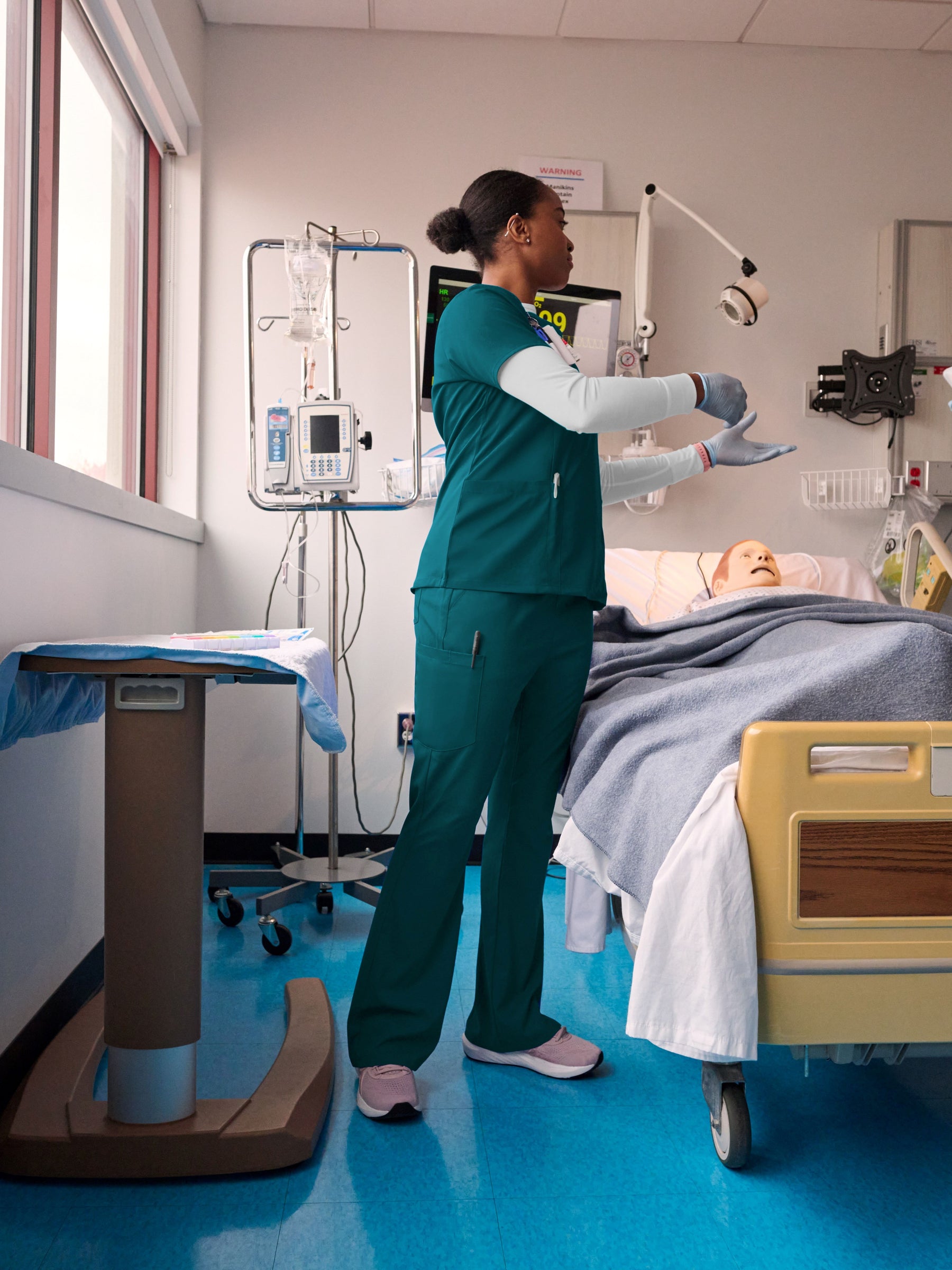 Nurse in caribbean scrubs attending to a patient in a hospital room with medical equipment.