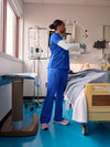 Nurse in blue scrubs attending to a patient in a hospital room.