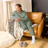 Woman sitting on a brown leather couch  in green lounge set using a tablet in a cozy living room.