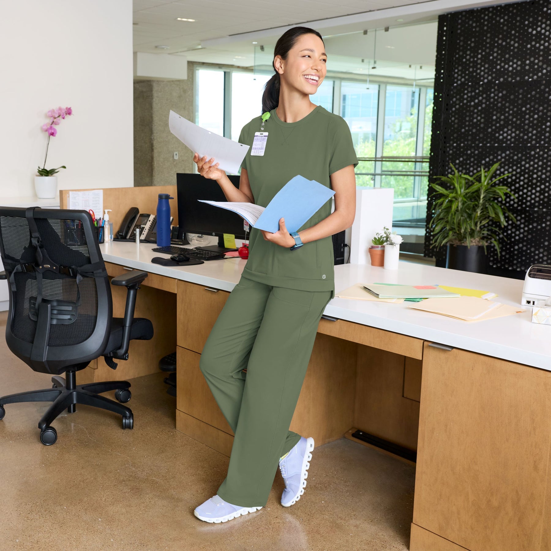 Person in olive green scrubs standing in a modern office setting