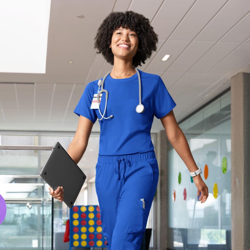 nurse in blue scrubs with a stethoscope, holding a tablet, in a hospital setting.