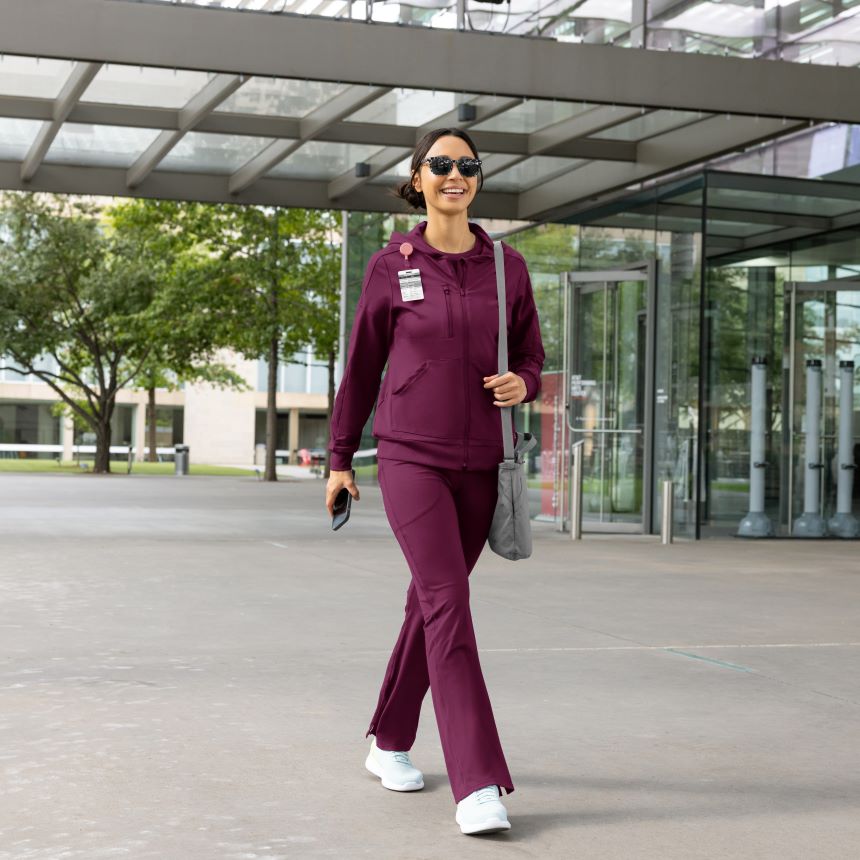 Woman in a wine medical scrubs set walking outdoors.